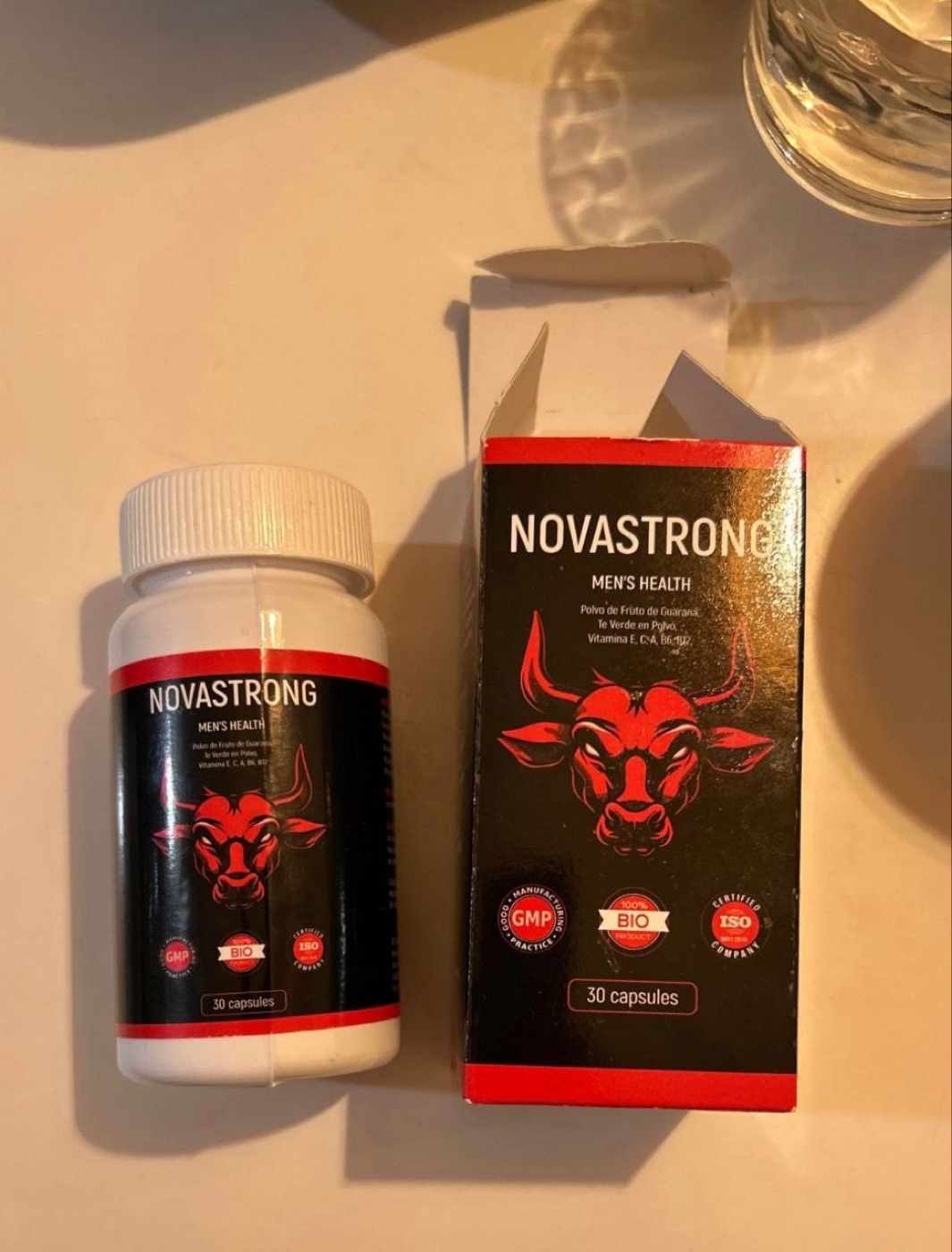 Frasco blanco y caja negra de NovaStrong con etiqueta del toro rojo